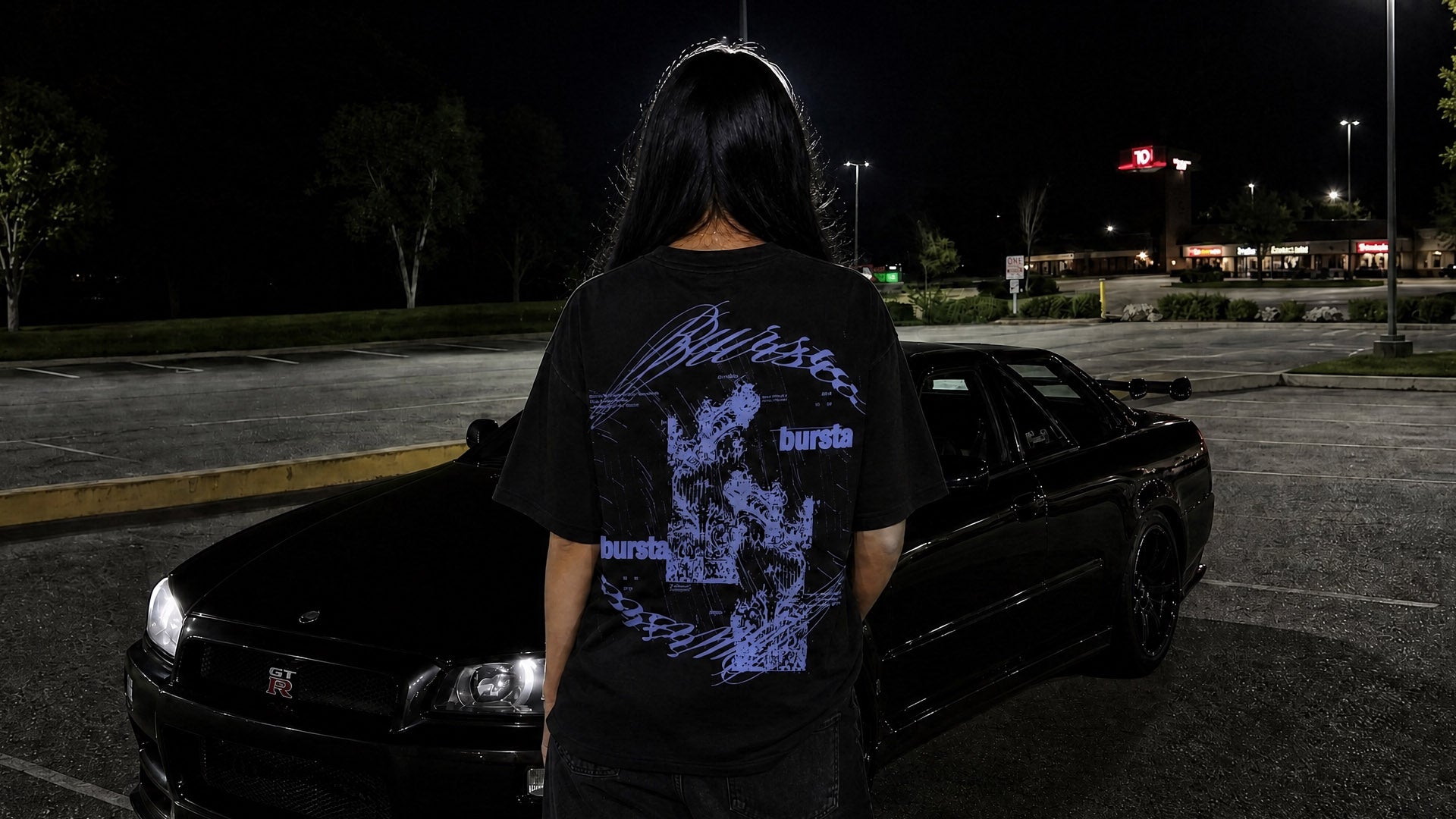 Person wearing the Bursta Eternal Tee in Ink Black standing next to a black car in a parking lot at night.